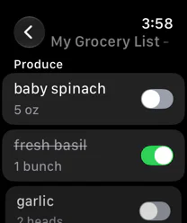 A grocery list open on Apple Watch: baby spinach, fresh basil crossed off as purchased, and garlic, each with a switch.